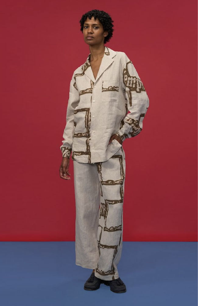 Woman wearing cream linen shirt and pants with chain print details against red and blue background