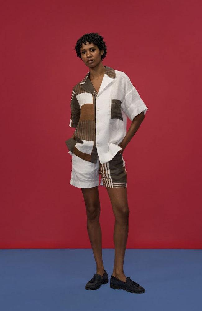 Model wearing Studio Afuera colorblock linen shirt with brown and white panels, paired with matching shorts, against vibrant red backdrop